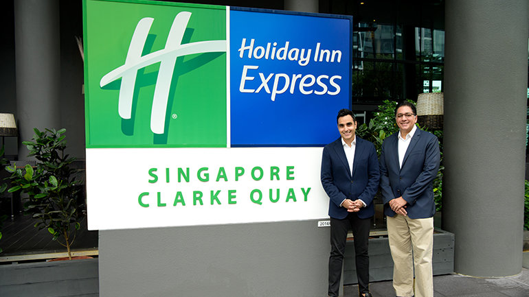 Image outside of the Holiday Inn Express Clarke Quay in Singapore. Image is outside a large Holiday Inn Express sign with Kishin RK, Founder and CEO of RB Capital Group and Vivek Bhalla, Managing Director, South East Asia & Korea, IHG Hotels & Resorts
