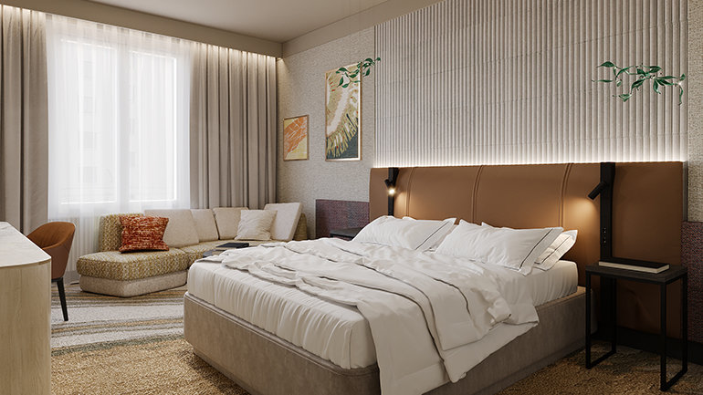 "A wide shot of a modern and stylish hotel guest room with a warm, neutral colour palette. In the centre-right, a large bed with crisp white linens sits against a textured, vertically ribbed feature wall. The bed has a brown leather, backlit headboard with built-in black reading lamps. To the left, a cozy beige L-shaped sofa with colourful throw pillows is positioned by a large window dressed in sheer and heavy beige curtains, allowing bright daylight to fill the room. The wall above the bed is decorated with framed artwork. The floor is covered in a patterned carpet in shades of gold, brown, and grey, and in the left foreground, the corner of a light wood desk and an orange chair are visible."