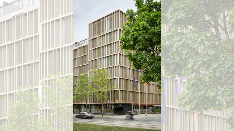 Exterior photo of the future Crowne Plaza Vienna, showcasing a contemporary multi-storey building with a striking vertical-fin façade in warm bronze tones, floor-to-ceiling windows, and a tree-lined streetside setting flanked by European, Austrian and city flags.