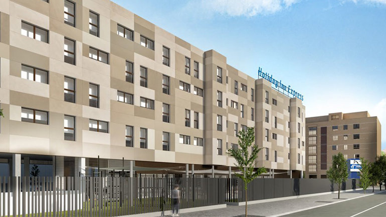 Design rendering of the Holiday Inn Express Madrid – Julián Camarillo exterior, featuring a large contemporary building with a neutral-toned façade, street-level fencing, landscaped surroundings, and hotel signage along an urban street.