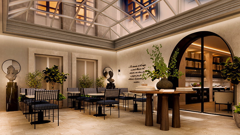 Elegant indoor courtyard restaurant with a glass atrium ceiling, cream stone walls and abundant greenery. The space features café-style seating, sculptural tables, classical busts and an arched entrance leading into a stylish dining area, blending contemporary hospitality design with Italian architectural influences. 
