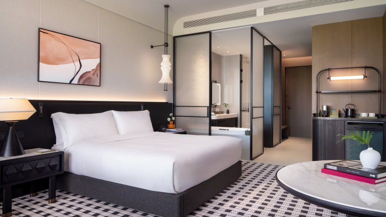 Modern guest room featuring a king bed with crisp white linens, dark wood furnishings, and contemporary lighting.