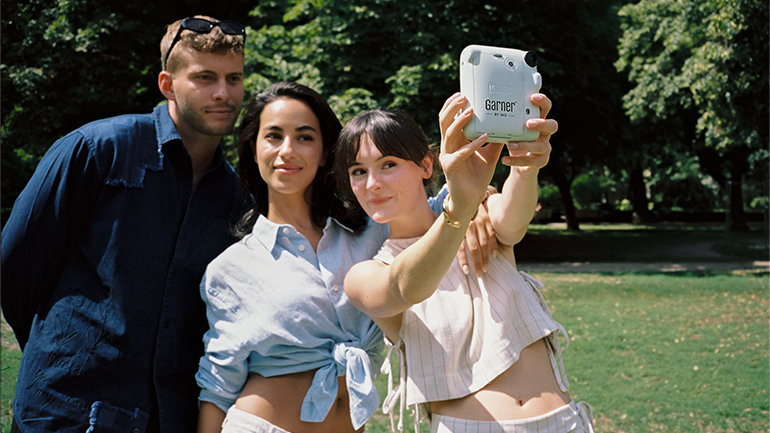 Three people take a photo with an instant camera in a park with trees in the background