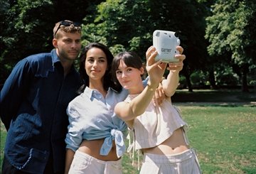 Three people take a photo with an instant camera in a park with trees in the background