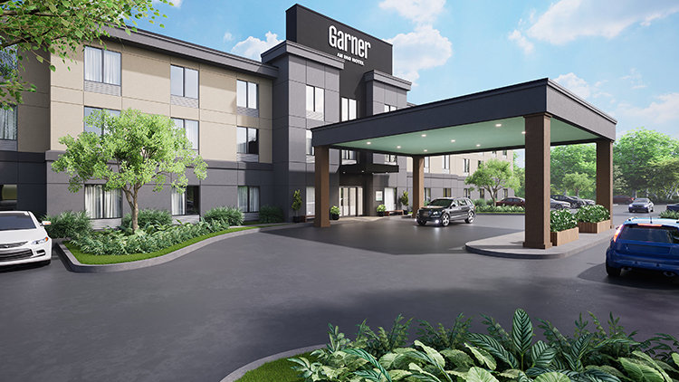 Modern exterior view of a Garner hotel, an IHG property, featuring a covered driveway entrance, parked cars, and landscaped greenery under a clear blue sky.