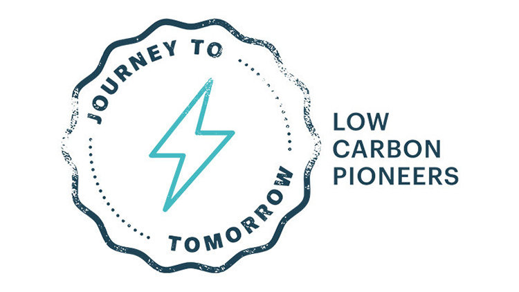 A white background features a circular logo with a jagged outline, containing the text “Journey to tomorrow” around a teal lightning bolt icon. To the right of the logo, in black capital letters, it reads “Low Carbon Pioneers”.